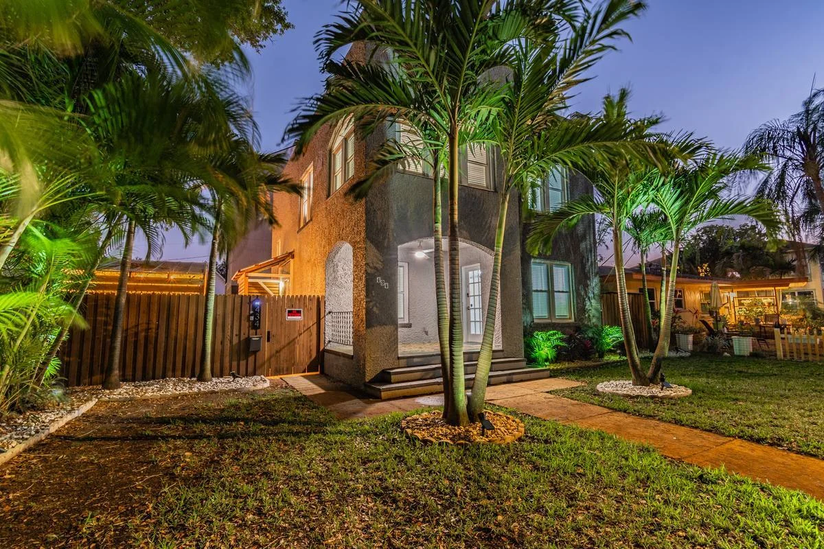 Twilight exterior of St. Pete bungalow with palm trees, arched doorway and green uplighting