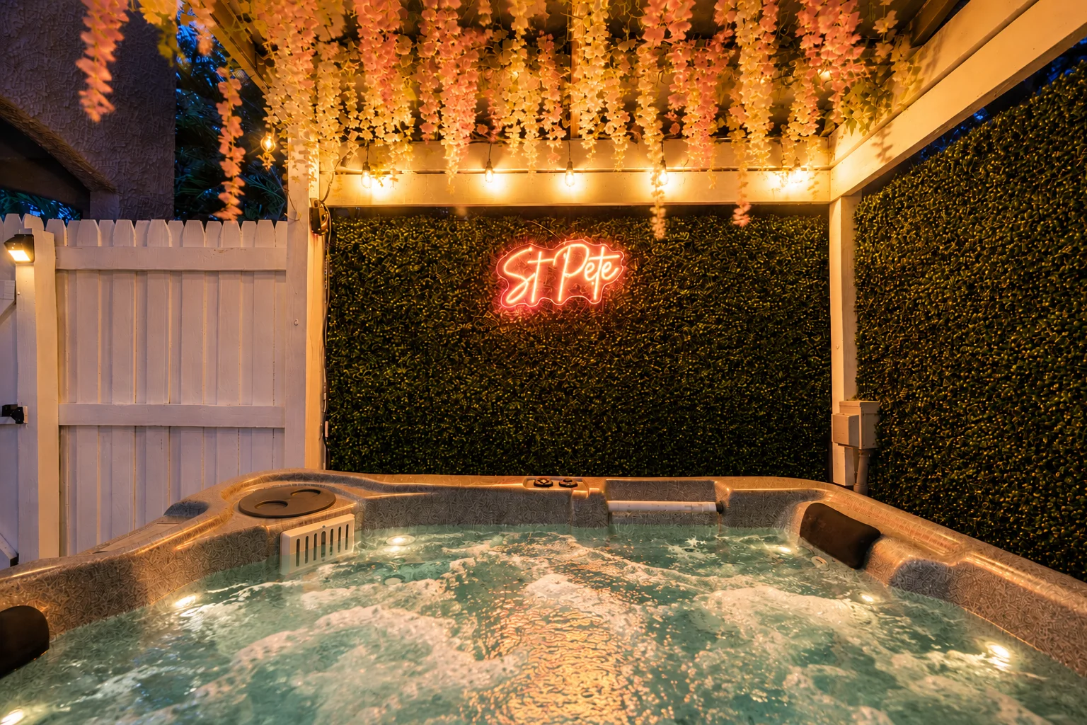 Private hot tub at night with glowing St Pete neon sign, hanging wisteria flowers and string lights at St. Pete bungalow